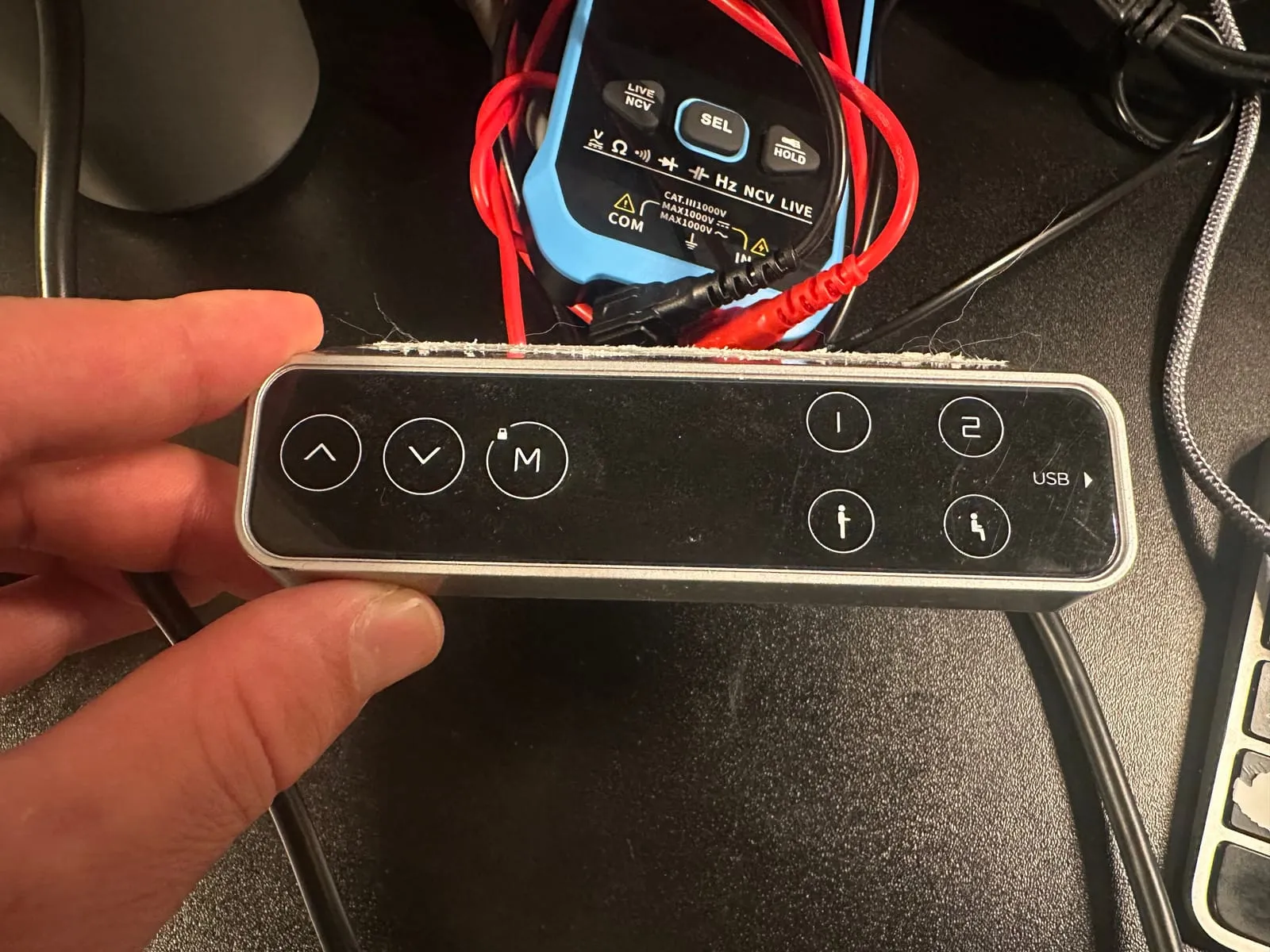 The desk’s handset held in a hand, with up, down and M keys on the left, a small lock icon above M, and memory, sit and stand keys on the right