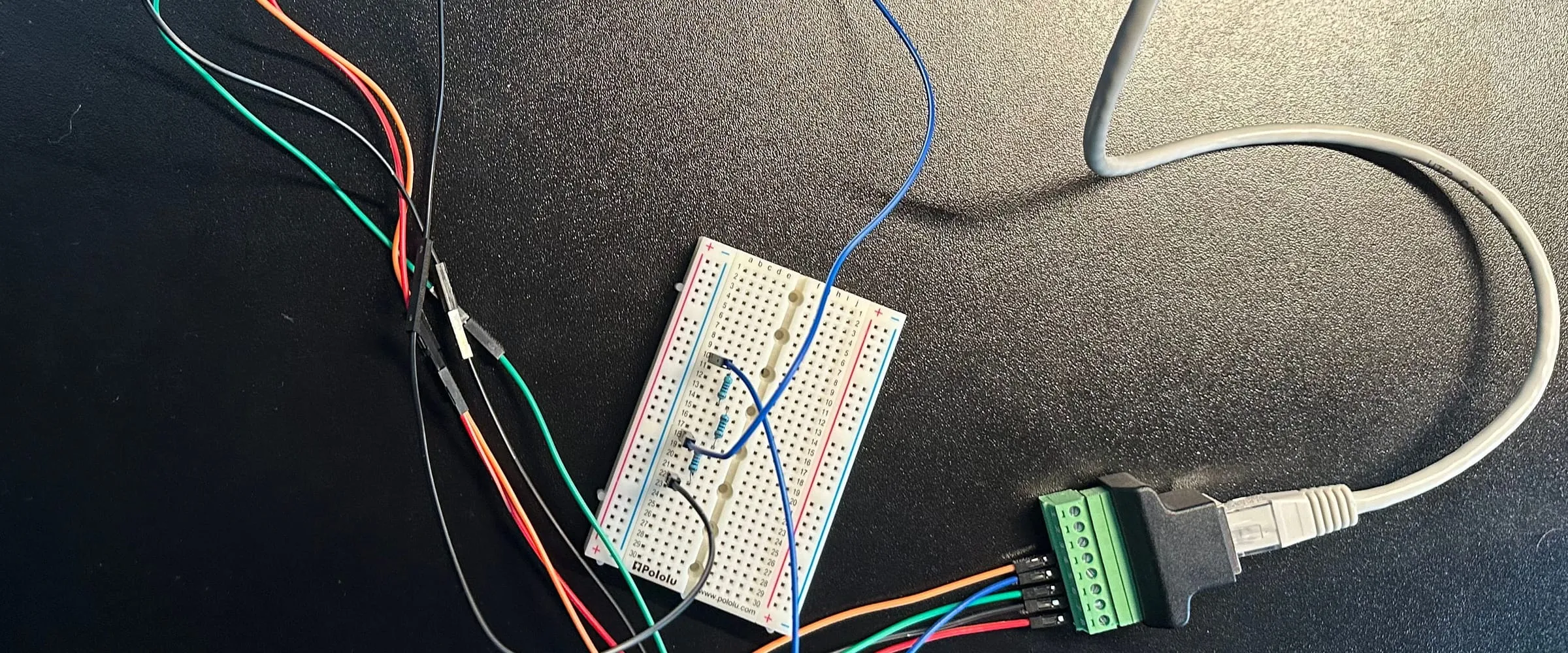 An RJ45 screw terminal, a breadboard with three resistors and colored jumper wires on a black desk